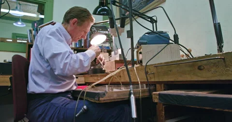 Low angle wide shot of an older male jeweler working on a belt buckle. Stock Footage 137268394