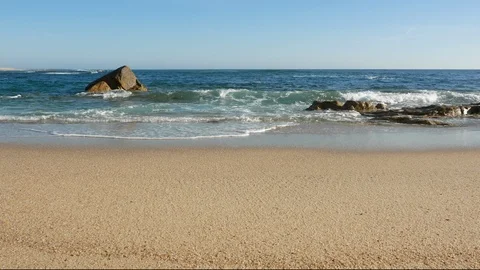 Low angle wide shot over empty beach as blue waves break on the sandy shore Stock Footage 108516930