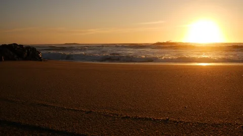 Low angle, wide view over sandy beach at sunset over ocean with sun on horizon Stock Footage 104682520