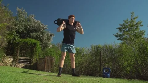 Low angle wide view of young man performing weighted sandbag squats on grass Stockbeeldmateriaal 336235947