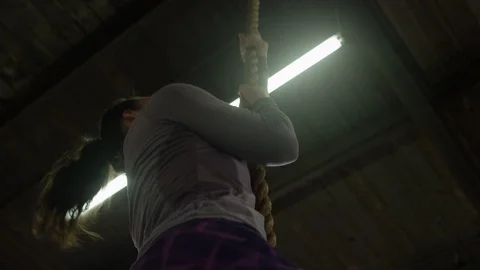 Low angle of young, fit caucasian woman climbing a rope in industrial-style gym 스톡 동영상 124455322