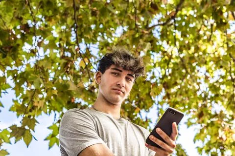 Low angle of a young man holding his smartphone, serious, looking at the ca.. Stock Photos