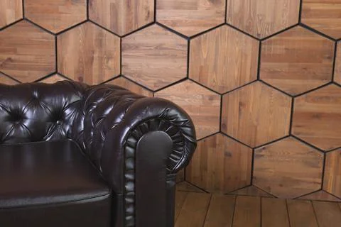 Low black leather sofa with a round armrest set on hexagon wood-panelled wall Stock Photos