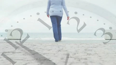 Low camera rising revealing senior woman walking to sea while clock hands Stock Footage 330192091