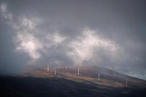 Low clouds and winter light play between bare hills and wind turbines Foto stock