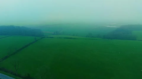 Low clouds drifting above green countryside pasture with grazing sheep below Video stock 333580325