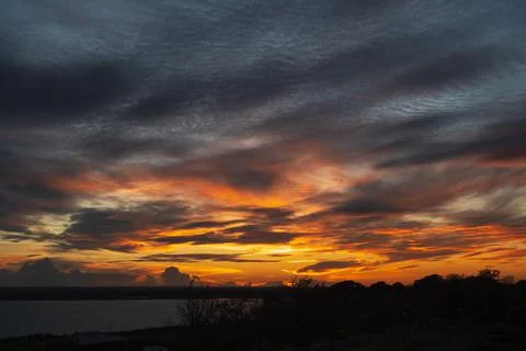 Low clouds forming a dramatic, fiery sky at sunset over water. Stock Photos