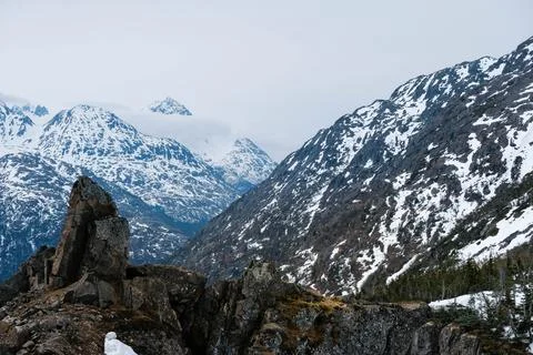 Low clouds hang over snow covered mountains with lichen covered and large s.. Stock Photos