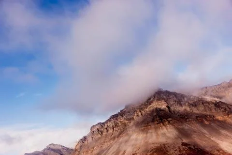 Low clouds hang at the top of of eroding red cliffs in the Brooks Range Foto stock