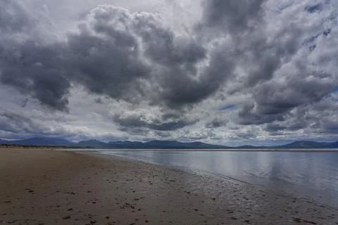 Low, dark clouds pass slowly across Llanddwyn beach at low tide. Foto stock