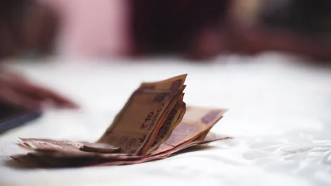 Low depth of feild shot of rupee notes lying on a table as an out of focus hand Stock Footage 144560496