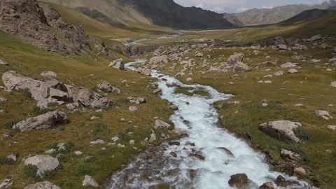 Low drone flight along a rushing alpine stream through a valley, Kyrgyzstan Stockbeeldmateriaal 347241589