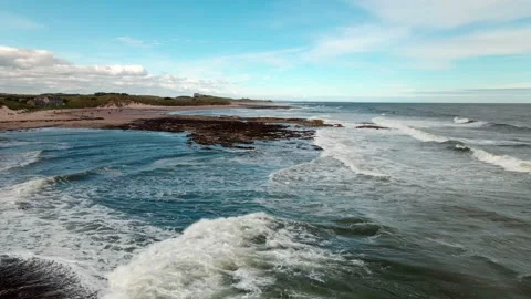 Low drone flight over waves and beach near Seahouses in Northumbria Stock Footage