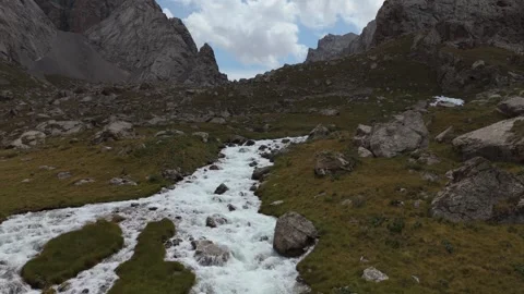 Low drone flight up a rushing stream toward rocky peaks, Kyrgyzstan Video stock 347241493