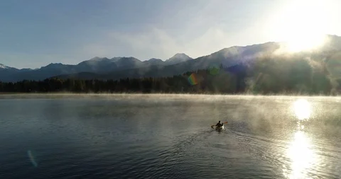 Low Drone Follow Shot Of A Man Paddling Across A Lake In The Mountains At Sunris Stock Footage 101045294