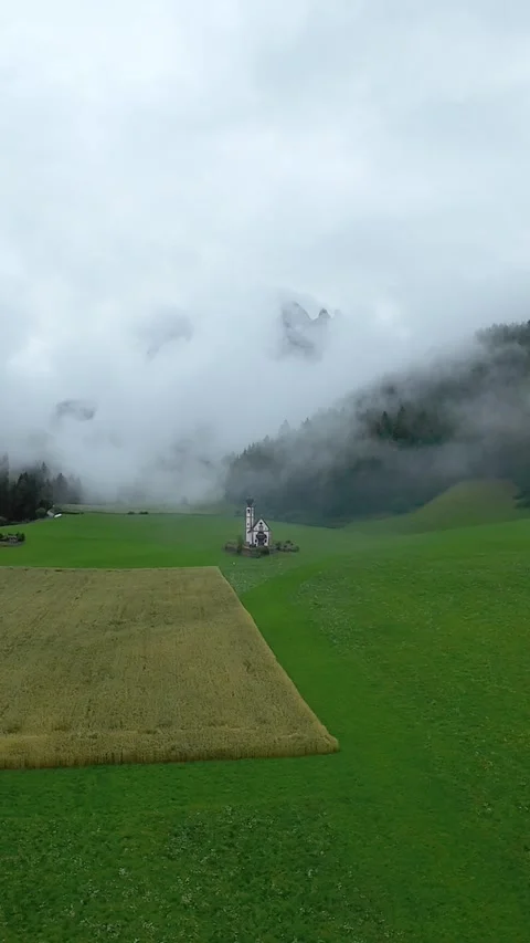 Low drone over crop rectangle in misty valley, harvested patch contrasts vivid Stockbeeldmateriaal 323778185
