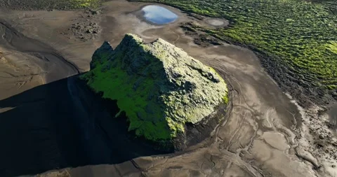 Low drone pass over a moss-covered volcanic hill rising from black sand plains Stock Footage 327806767