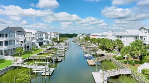 Low, drone push in footage, flying past houses over a coastal canal.  스톡 동영상 269431905