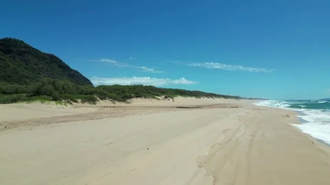 Low drone view along a sandy beach with surf and hills in Hawaii Stockbeeldmateriaal 348263753