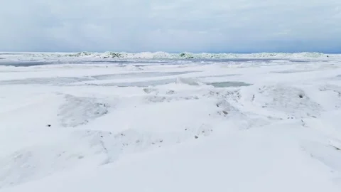 Low drone view over frozen sea with a dark open-water lead and wind-swept snow Stock Footage 332091571