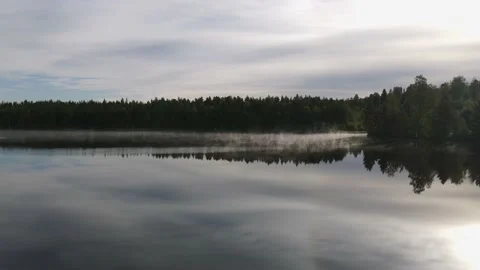 Low drone view of a reflective, calm and foggy lake one early summer morning. Stock Footage 145870350