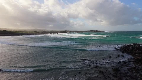 Low early evening flight over extensive beach out to sea with rolling white 스톡 동영상 331116623