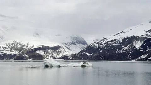 Low flat iceberg glides past avalanche-furrowed peaks in Glacier Bay Stock Footage 336220058