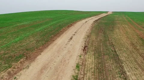 Low flight above green fields and dirt road, aerial panoramic view. 動画素材 56206796