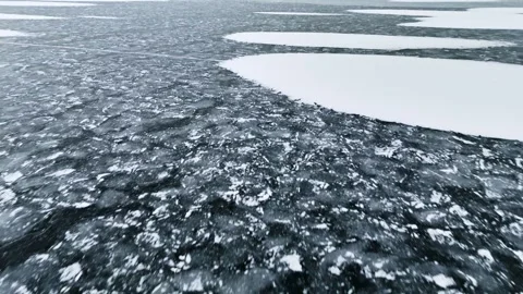 Low flight over dark frozen ice with white snow patches and a long crack line Stock Footage 332096693