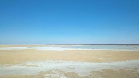 Low flight over sandy grassland with water in shallow pan Stock Footage 80599044