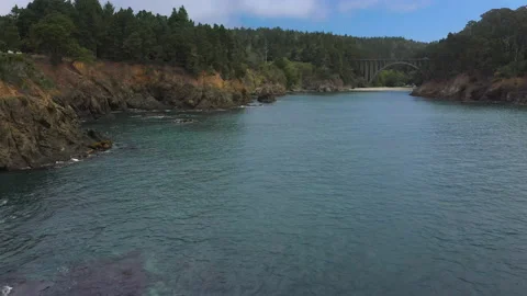 Low flight over water towards a beach with a bridge above Stock Footage 152890202