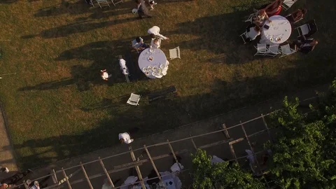 Low flight shot over people sitting at tables moving on green lawn at open party Stock Footage 86493830