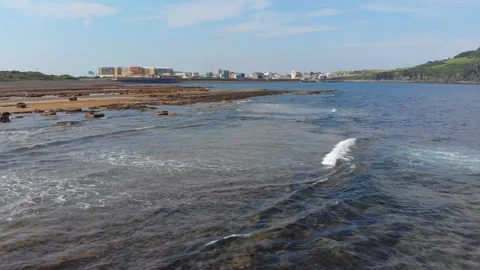 Low flying drone over rocks and sea towards town Stock Footage 91092235