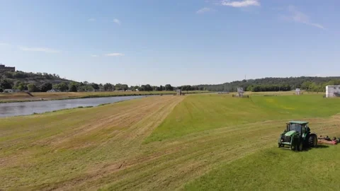 Low flying drone shot of tractor cutting field of grass by the river Stock Footage 135472120