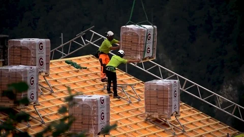 Low flying helicopter delivering construction equipment cargo to rooftop nearby Stock Footage 79810496