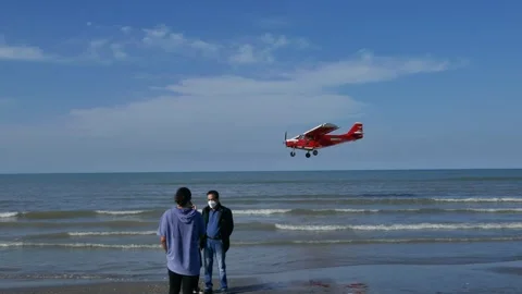 Low-flying red bush plane illegally skims low above a seaside crowd and boats Stock Footage 320744965
