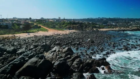 Low forward flight over massive dark boulder field with waves lapping the edges Видео 332687089