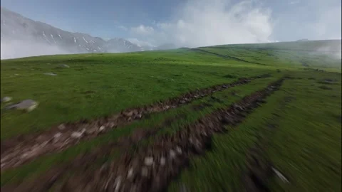 Low FPV flight over lush green landscape with mountains and clouds in view Stock Footage 341358056