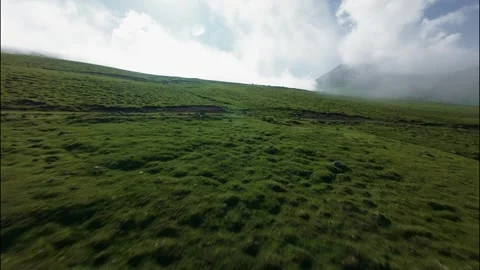 Low FPV flight over lush green hillside with clouds and distant mountains Stock Footage 341475232