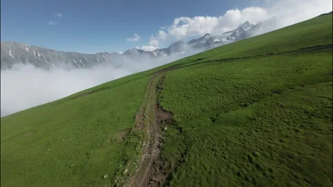 Low FPV flight over lush green hillside with mountains and clouds in background Stock Footage 341475237