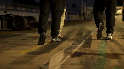 Low handheld shot of three car drivers walking along the race track in the Stock Footage 98381006