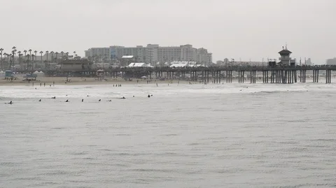 Low to high slow-mo 4k aerial of surfers in ocean and crowds of people on pier Stock Footage 122093105