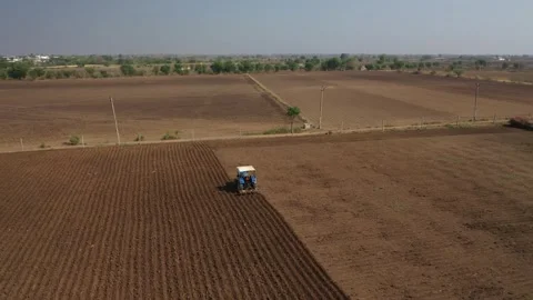 Low horizon wide drone perspective following a blue tractor pulling a disc Video stock 337191720