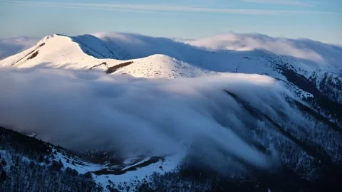 Low inversion clouds drift over snow-capped mountain peaks and hills Stock Footage 268602617
