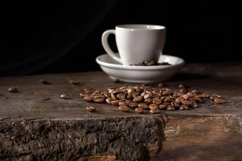 Low key image of a white coffee cup surrounded by scattered coffee beans Stock Photos
