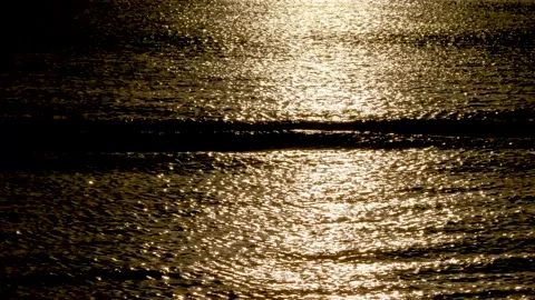 Low key light. Waves smoothly rolling with sunset light reflecting in the wat Stock Footage 132779477