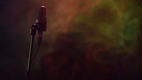 Low-key shot of microphone stand with colorful smoke in background Video stock 105667865