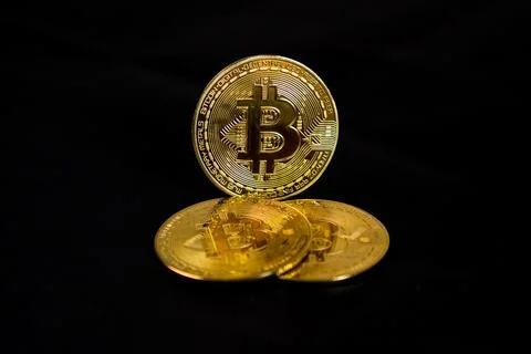 A low-key three physical golden Bitcoin token coins arranged over a solid b.. Stock Photos