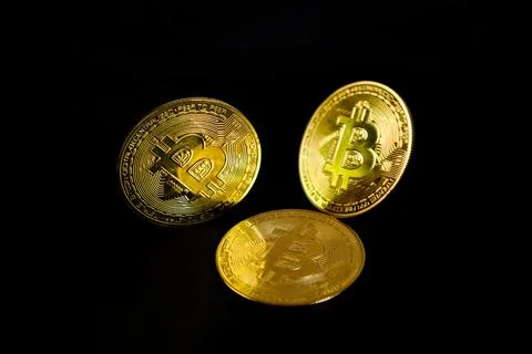 A low-key three physical golden Bitcoin token coins arranged over a solid b.. Stock Photos