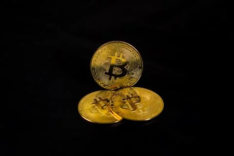 A low-key three physical golden Bitcoin token coins arranged over a solid b.. Stock Photos